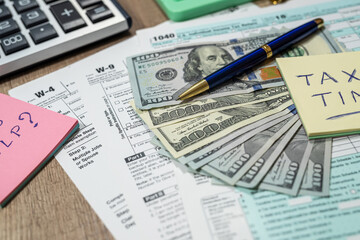 tax forms 1040 are blank to fill out and dollars are sloppily scattered on a wooden table.