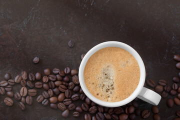 white cup of coffee with coffee beans on a dark background. view from above
