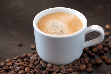 white cup of coffee with coffee beans on a dark background. close-up