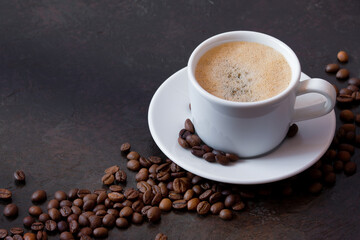 white cup of coffee on a saucer with coffee beans on a dark background