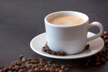 white cup of coffee on a saucer with coffee beans on a dark background. front view