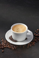 white cup of coffee on a saucer with coffee beans on a dark background. vertical image