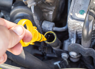 A man's hand takes out an oil dipstick in a diesel car engine to check the level and quality of engine oil. Oil change service interval, worker