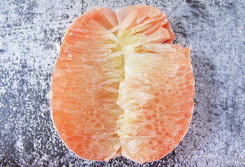 Close up photo of a juicy pink pomelo segment cut in a half in rusty background