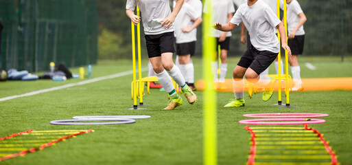 Teenage Football Players Running in Two Rows on Training Camp. Young Boys Running Slalom Track Between Training Poles and Jumping Over Ladders. Soccer Training Equipment