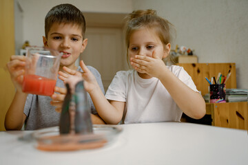 Children, boy and a girl are conducting an experiment with a volcanic eruption at home.
