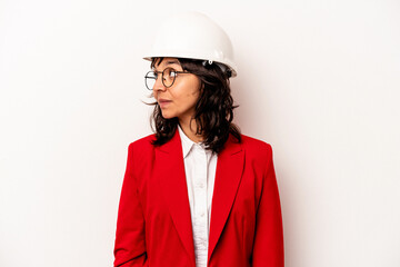 Young architect hispanic woman with helmet isolated on white background looks aside smiling, cheerful and pleasant.