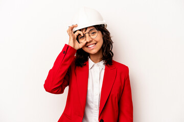 Young architect hispanic woman with helmet isolated on white background excited keeping ok gesture on eye.