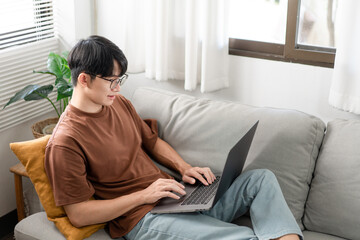 Obraz premium Technology Concept The man that is putting on glasses leaning his back on the dark yellow while focusing on the laptop’s screen