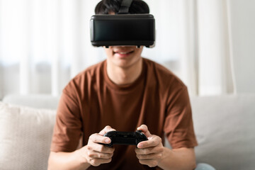 Technology Concept A person wearing a virtual reality headset and holding a black console game while sitting on the sofa