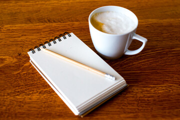 Top view of open school notebook with blank pages, coffee cup and pencil on wood table background. Flat lay, creative workspace office. Business-education concept with copy space. 