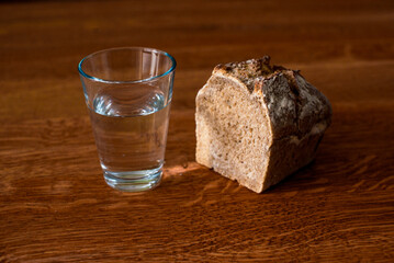 A glass of water and a loaf of bread on a wooden table. Fasting for bread and water to strengthen the spirit. Lent. Easter. Prison food. Food for poor.