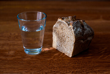 A glass of water and a loaf of bread on a wooden table. Fasting for bread and water to strengthen the spirit. Lent. Easter. Prison food. Food for poor.