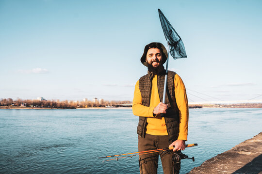 Image of fisherman holding fishing rod  and fishing net while standing by a river.