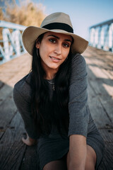 Close up portrait of a beautiful Hispanic woman wearing a hat sitting on a dock by the river close up