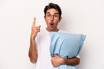 Young caucasian man wearing pajamas holding a pillow isolated on white background having some great...