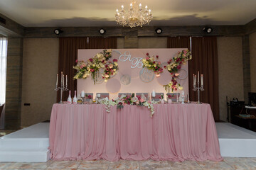 Decorated pink wedding presidium, festive table and arch for just married, event organization. Beautiful flowers and burning candles.