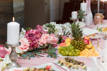 Obraz na płótnie Canvas Beautiful festive table with white burning candles and pink flowers, exotic fruit cut. Valentines day romantic dinner or just married wedding presidium.