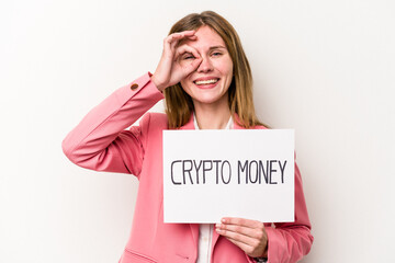 Young English business woman holding a crypto money placard isolated on white background excited keeping ok gesture on eye.