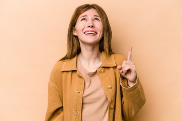 Young English woman isolated on beige background indicates with both fore fingers up showing a...
