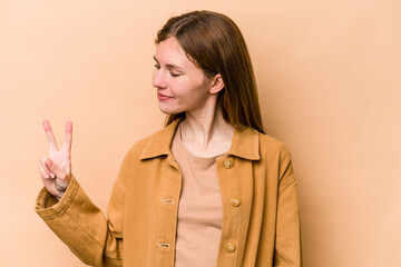 Young English woman isolated on beige background joyful and carefree showing a peace symbol with fingers.