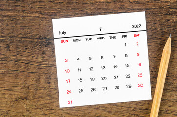 July 2022 calendar and wooden pencil on vintage wooden background.