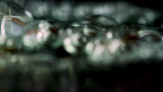 Close up of boiling wayer with moving air bubbles on a black background. Stock footage. Concept of cooking or making hot beverage.