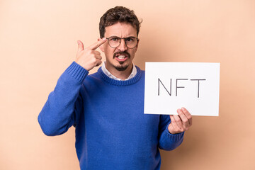 Young caucasian man holding a NFT placard isolated on beige background showing a disappointment...