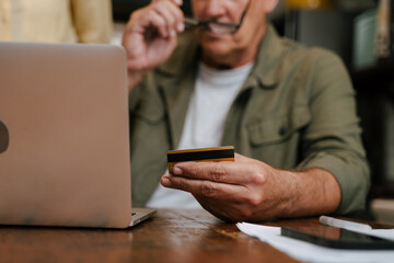 close up of credit card while elderly male online shopping from home 