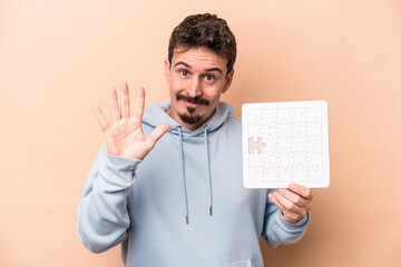 Young caucasian man holding a puzzle isolated on beige background smiling cheerful showing number...