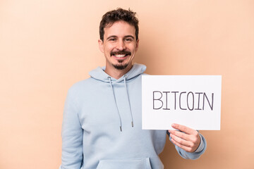 Young caucasian man holding a bitcoin placard isolated on beige background happy, smiling and cheerful.