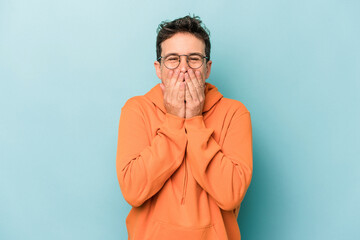 Fototapeta na wymiar Young caucasian man isolated on blue background laughing about something, covering mouth with hands.