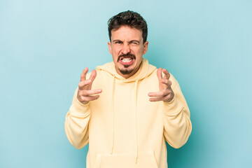 Young caucasian man isolated on blue background upset screaming with tense hands.