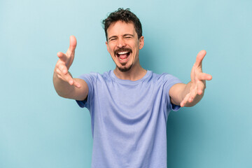 Naklejka premium Young caucasian man isolated on blue background feels confident giving a hug to the camera.