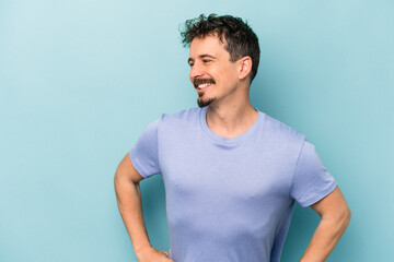 Young caucasian man isolated on blue background confident keeping hands on hips.