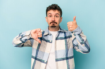Young caucasian man isolated on blue background showing thumbs up and thumbs down, difficult choose...