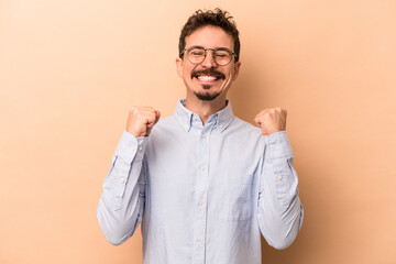 Young caucasian man isolated on beige background celebrating a victory, passion and enthusiasm, happy expression.