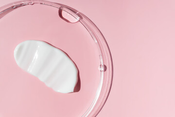 White cosmetic face cream texture in petri dish. Lotion smear on pink background. Beauty skincare...