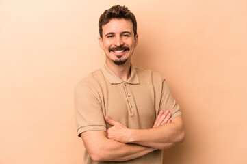 Young caucasian man isolated on beige background who feels confident, crossing arms with determination.