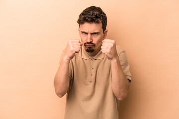 Young caucasian man isolated on beige background showing fist to camera, aggressive facial expression.
