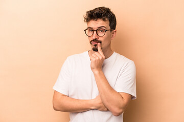 Young caucasian man isolated on beige background contemplating, planning a strategy, thinking about...