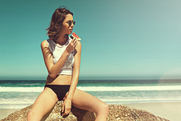 She makes eating healthy look so good. Cropped shot of a young woman enjoying a slice of watermelon on the beach.