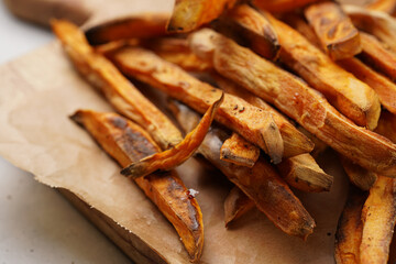 Healthy homemade oven baked sweet potato fries on a baking parchment, wooden board, with ketchup sauce