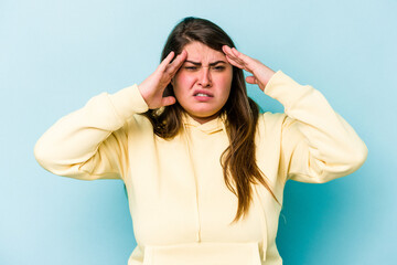 Young caucasian overweight woman isolated on blue background touching temples and having headache.
