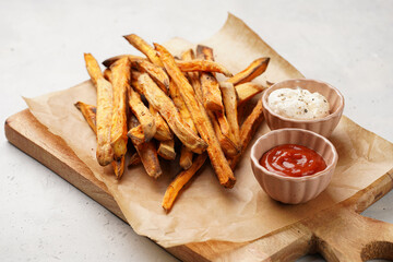 Healthy homemade oven baked sweet potato fries on a baking parchment, wooden board, with ketchup...