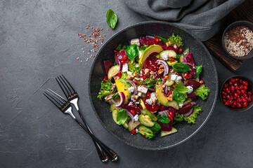 Vegetable salad with beetroot, avocado, cucumber, pomegranate and feta on a dark gray background. Healthy food. Top view, copy space.