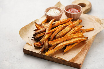 Healthy homemade oven baked sweet potato fries on a baking parchment, wooden board, with ketchup sauce and mayonnaise