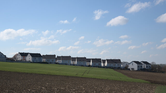 A row of newly built semi- detached houses on the horizon with blue cloudy sky.
