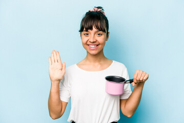 Young hispanic woman holding a saucepan isolated on blue background smiling cheerful showing number five with fingers.