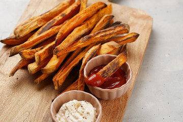 Healthy homemade oven baked sweet potato fries on a baking parchment, wooden board, with ketchup...